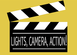 A camera clap board with "Lights, Camera, Action!" written on it.